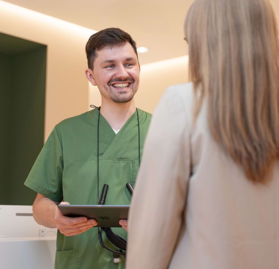 Fotoaufnahme: Zahnarzt Christopher Schwenn lächelt vor dem Empfang eine Patientin an